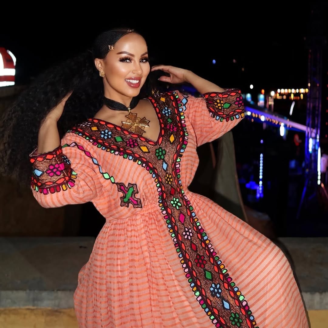 Woman in a colorful dress with intricate patterns at night. Gold Sand Ethiopian & Eritrean Axum Habesha Dress Ethgebya