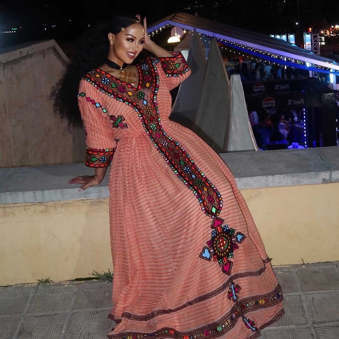 Woman in a traditional embroidered dress posing outdoors at night. Gold Sand Ethiopian & Eritrean Axum Habesha Dress Ethgebya