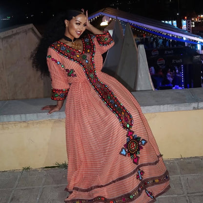Woman in a traditional embroidered dress posing outdoors at night. Gold Sand Ethiopian & Eritrean Axum Habesha Dress Ethgebya