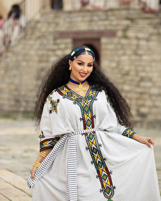 Woman in traditional attire with a colorful headscarf and jewelry, standing outdoors.