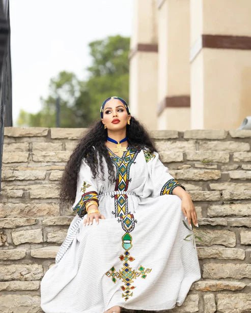 Woman in a white dress with colorful embroidery sitting on stone steps.
