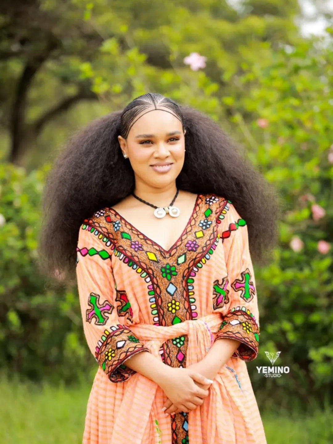 Woman in a colorful dress standing outdoors with greenery in the background Gold Sand Ethiopian & Eritrean Axum Habesha Dress Ethgebya