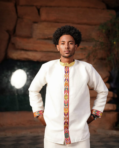 Man wearing a traditional outfit with a colorful tie against a rustic background .. Modern Habesha Men’s Shirt New Elegant Ethiopian Traditional Wear ethgebya gebeya