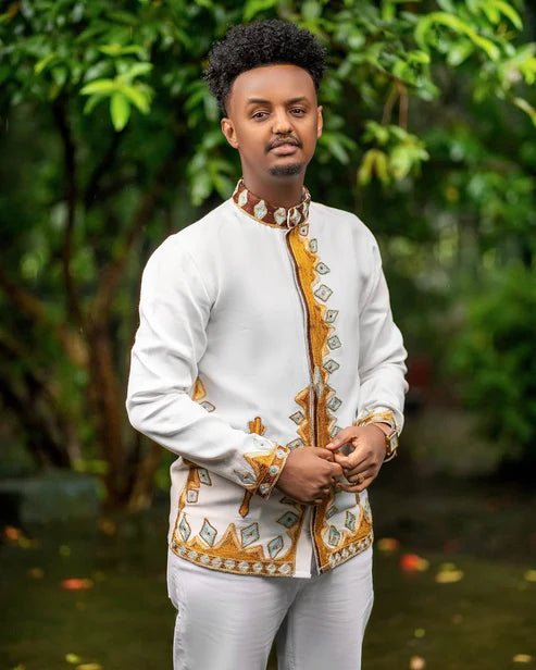 Man wearing a traditional outfit with white and gold patterns in a natural setting
