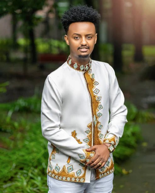 Man wearing a traditional embroidered jacket outdoors with greenery in the background
