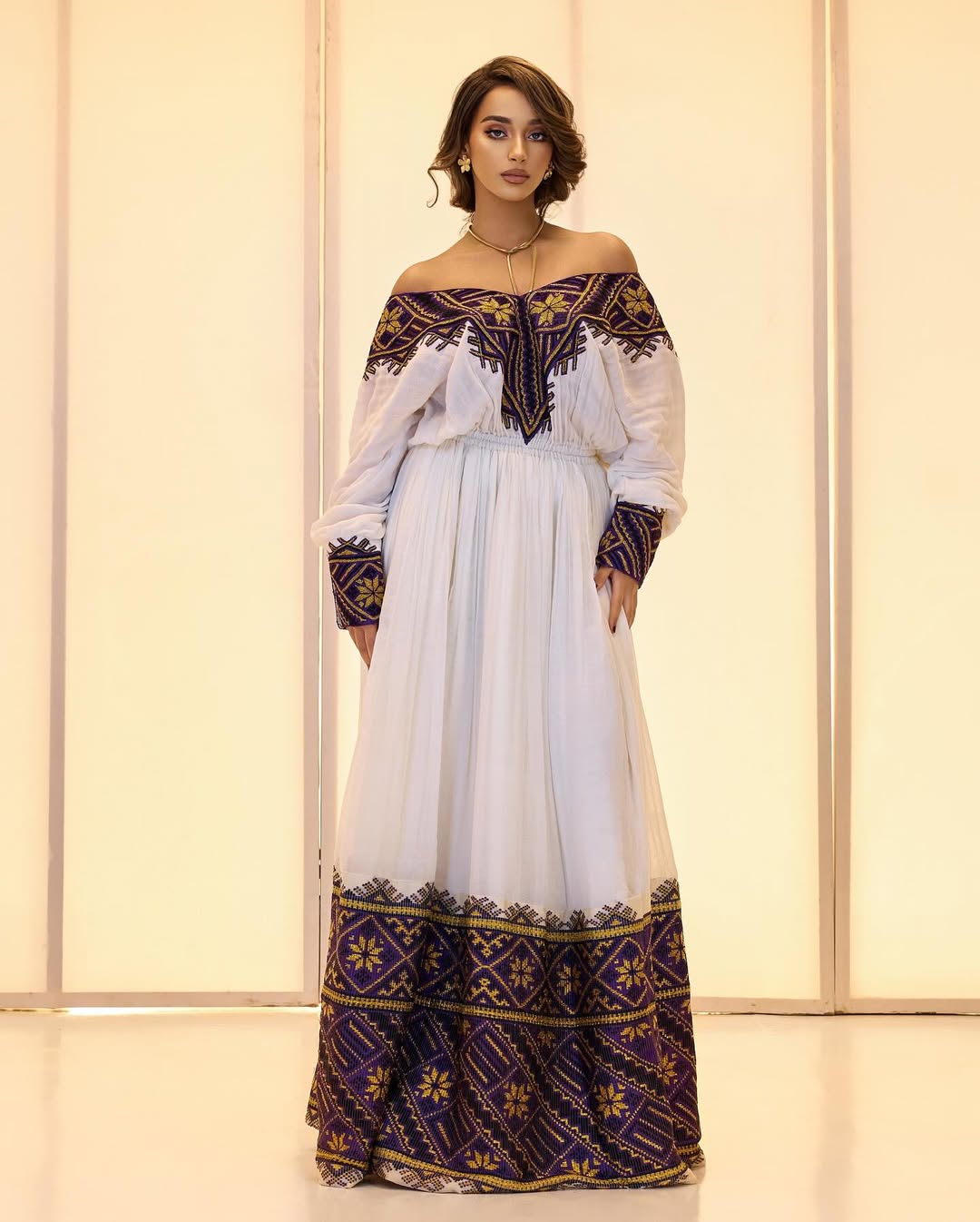 Woman wearing a white dress with black and gold embroidery against a light background
