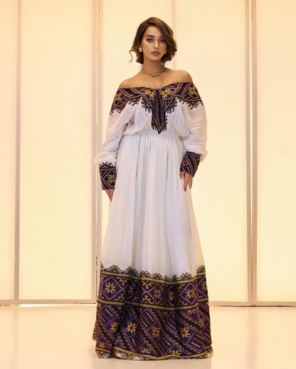Woman wearing a white dress with black and gold embroidery against a light background