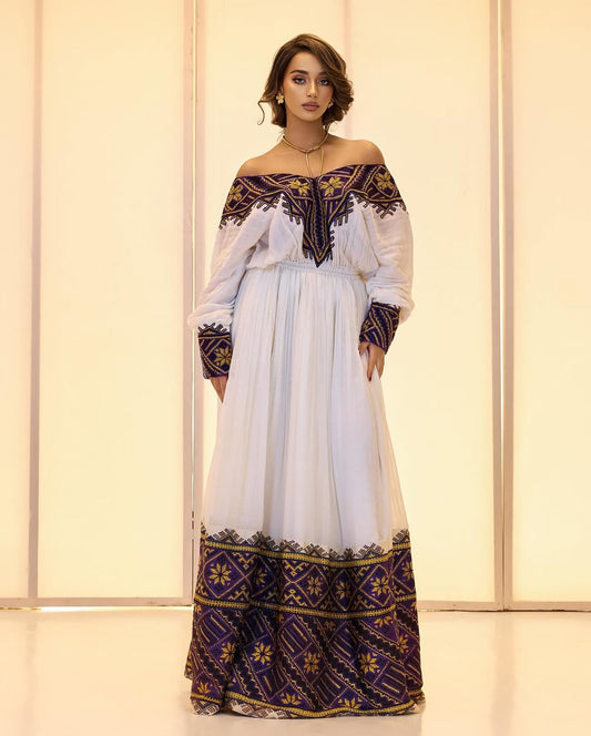 Woman wearing a white dress with black and gold embroidery against a light background