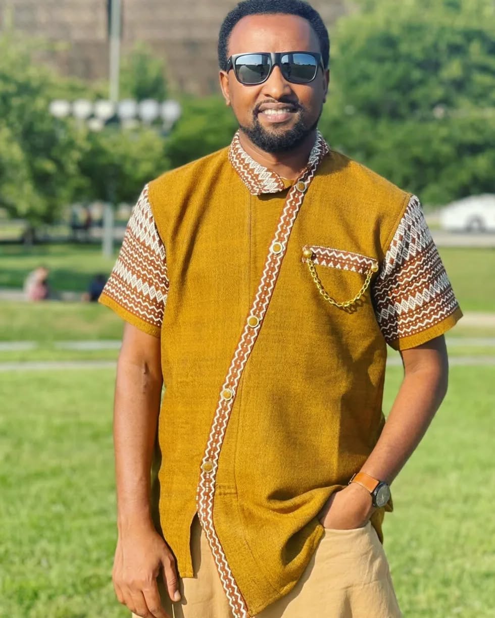 Man wearing a mustard yellow traditional outfit with sunglasses in an outdoor setting. Brown Modern Habesha Men’s Shirt Stylish Ethiopian Traditional Wear ethgebya gebeya usa habesha men