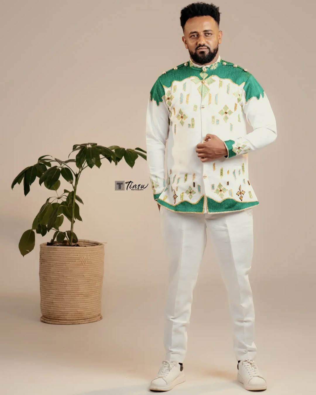 Man wearing a traditional outfit with green and white patterns, standing next to a potted plant on a beige background. Green Luxury Habesha Men’s Shirt New Modern Ethiopian Attire ethgebya gebeya usa habesha