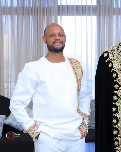 Man wearing a traditional outfit with intricate patterns in a room with white curtains. Golden Modern Habesha Men’s Shirt Ethiopian Traditional Clothing ethgebya gebya 