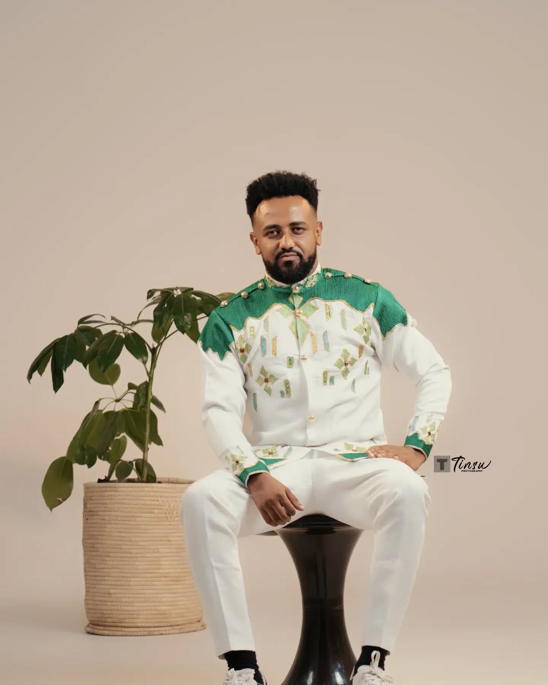 Man in a green and white outfit sitting on a black stool with a plant in the background Green Luxury Habesha Men’s Shirt New Modern Ethiopian Attire ethgebya gebeya usa habesha