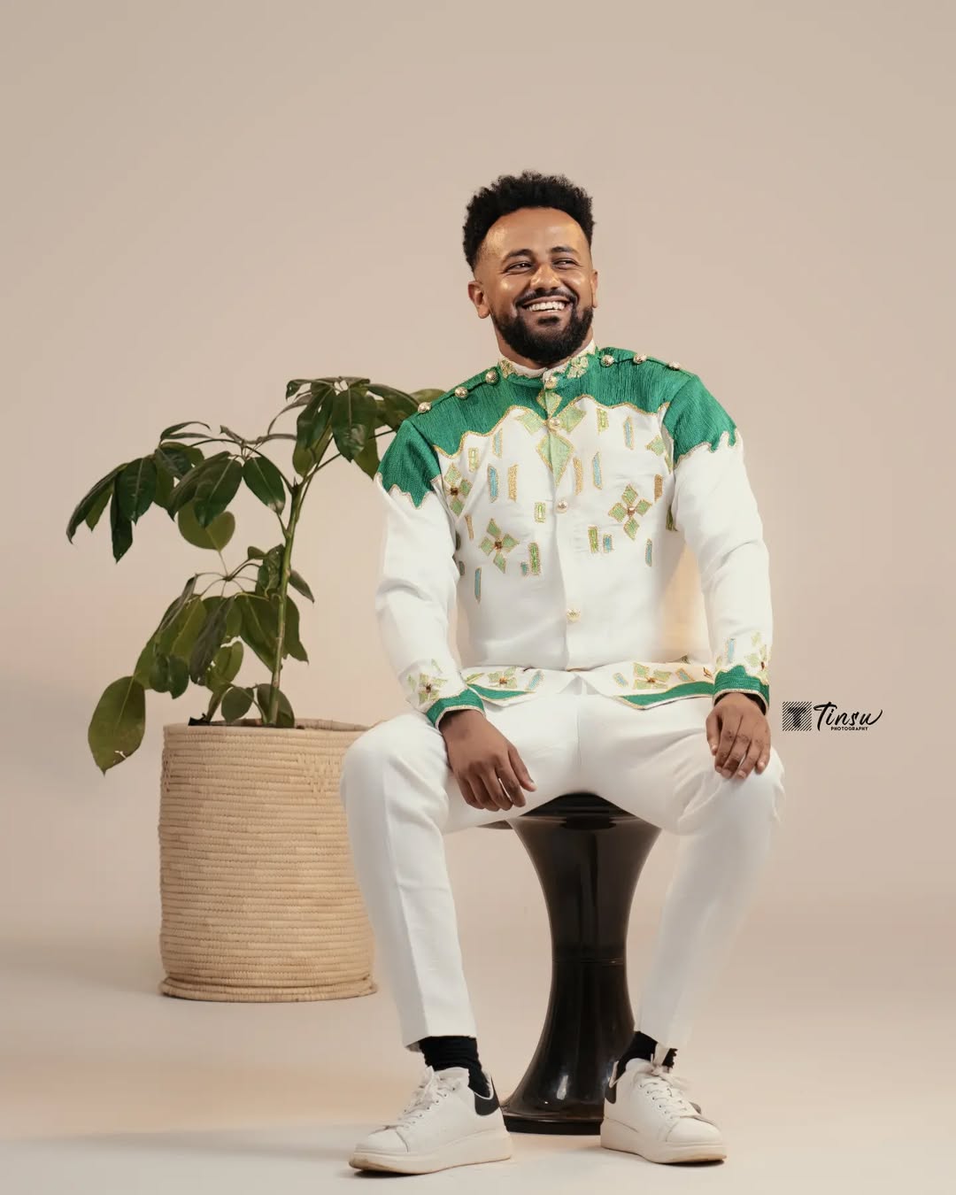 Man in traditional attire sitting on a black stool with a plant in the background Green Luxury Habesha Men’s Shirt New Modern Ethiopian Attire ethgebya gebeya usa habesha