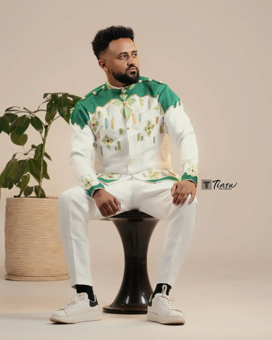 Man in a green and white outfit sitting on a black stool with a plant in the background. Green Luxury Habesha Men’s Shirt New Modern Ethiopian Attire ethgebya gebeya usa habesha