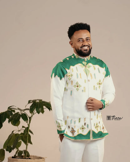 Man wearing a traditional outfit with green and white patterns, standing next to a plant on a beige background. Green Luxury Habesha Men’s Shirt New Modern Ethiopian Attire ethgebya gebeya usa habesha