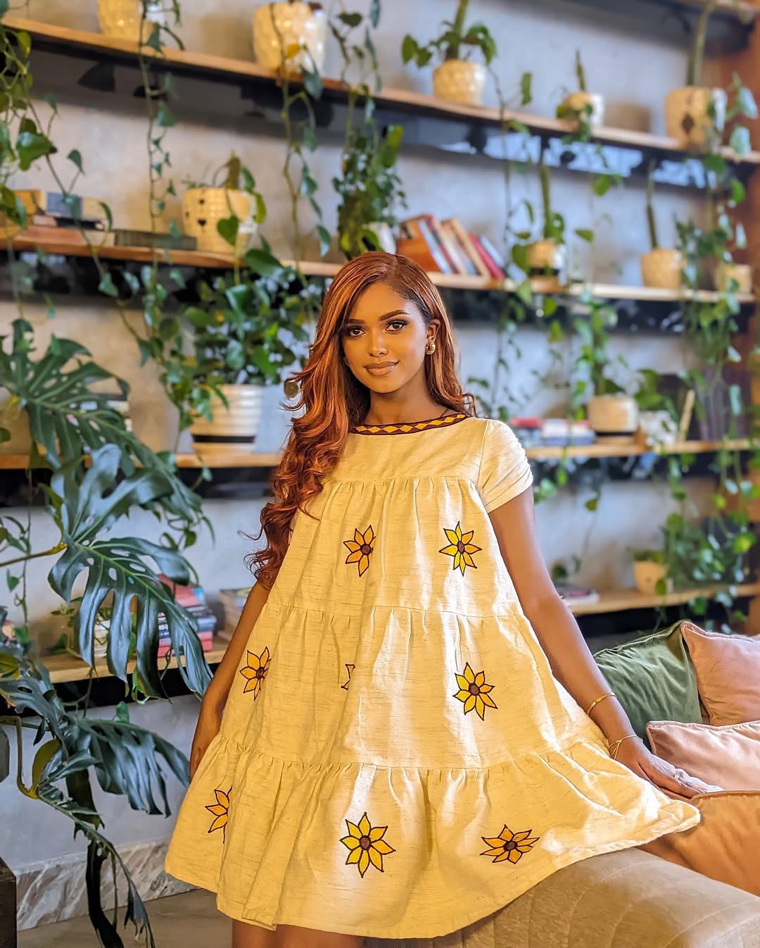 Woman in a yellow dress with floral patterns standing in a room with plants and shelves. Lightweight Short Habesha Dress Modern Summer Ethiopian Kemis ethgebya gebeya habesha kemis usa
