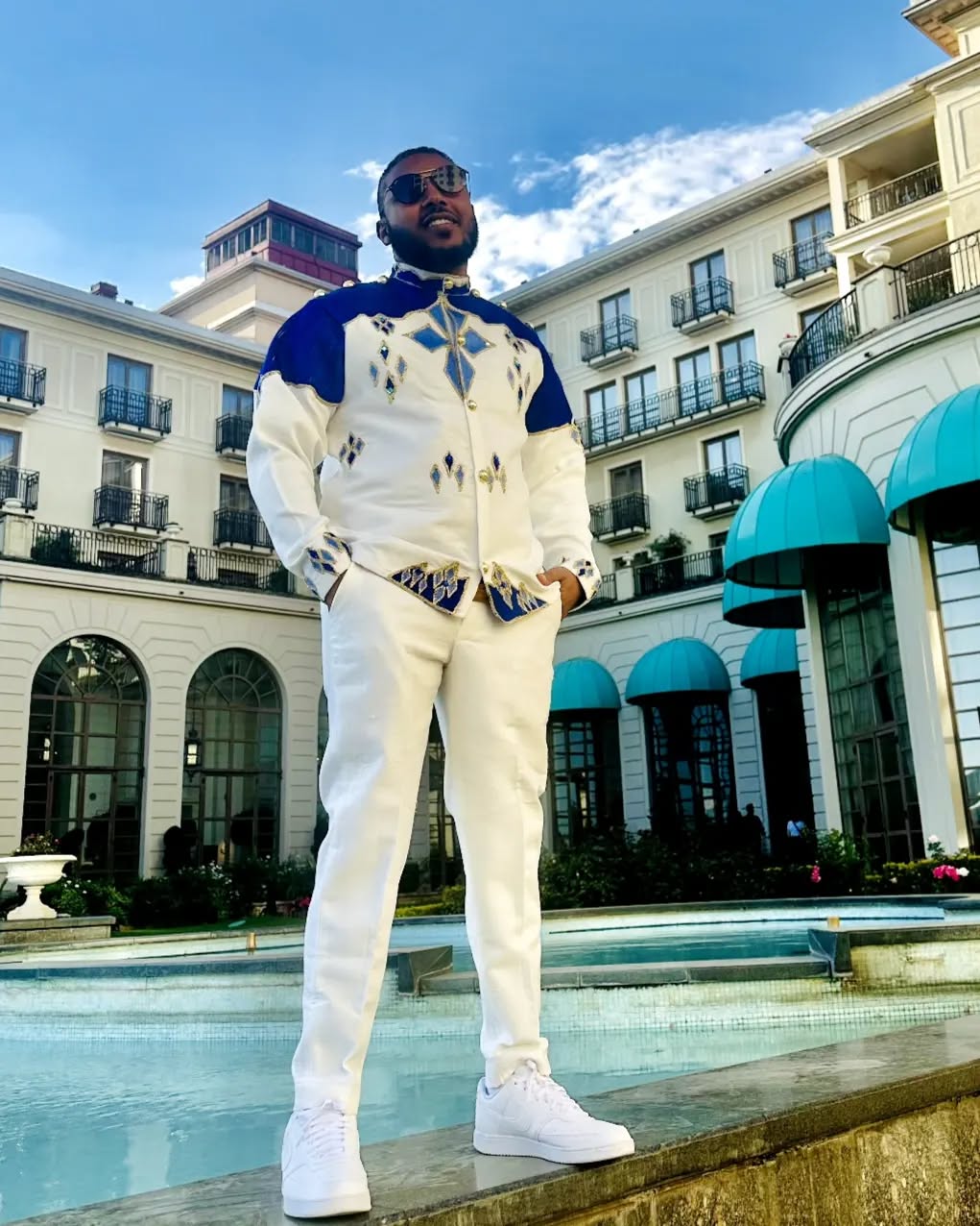 Man in a stylish outfit standing in front of a building with a pool. Blue Habesha Men’s Shirt New Modern Ethiopian Traditional Wear ethgebya gebeya usa habesha mens