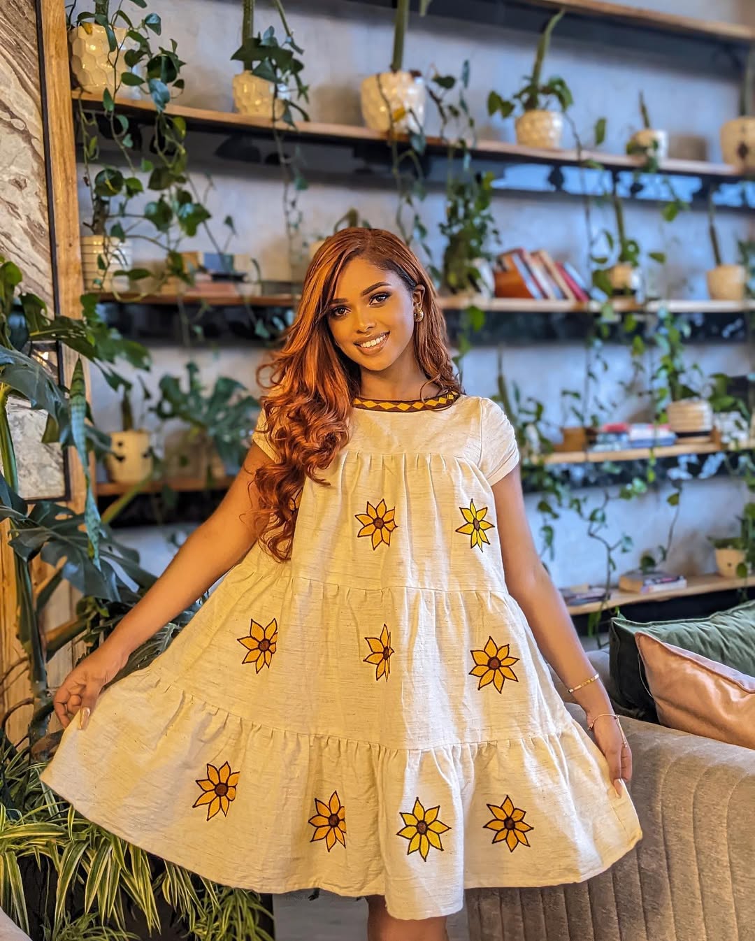 Woman in a yellow dress with floral patterns standing in a plant-filled room. Lightweight Short Habesha Dress Modern Summer Ethiopian Kemis ethgebya gebeya habesha kemis usa