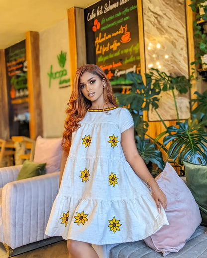 Woman in a white dress with yellow floral patterns sitting in a cozy cafe. Lightweight Short Habesha Dress Modern Summer Ethiopian Kemis ethgebya gebeya habesha kemis usa