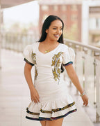Woman wearing a white dress with gold embroidery in an outdoor setting Modern Ethiopian Couple Set Mini Dress & Men’s Habesha Shirt ethgebya gebeya usa habesha kemis mini
