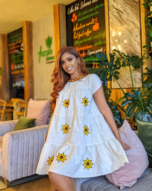 Woman in a white dress with yellow floral patterns in a cozy indoor setting. Lightweight Short Habesha Dress Modern Summer Ethiopian Kemis ethgebya gebeya habesha kemis usa