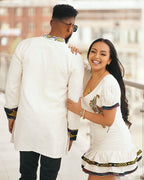 Couple in traditional attire standing close together outdoors. Modern Ethiopian Couple Set Mini Dress & Men’s Habesha Shirt ethgebya gebeya usa habesha kemis mini