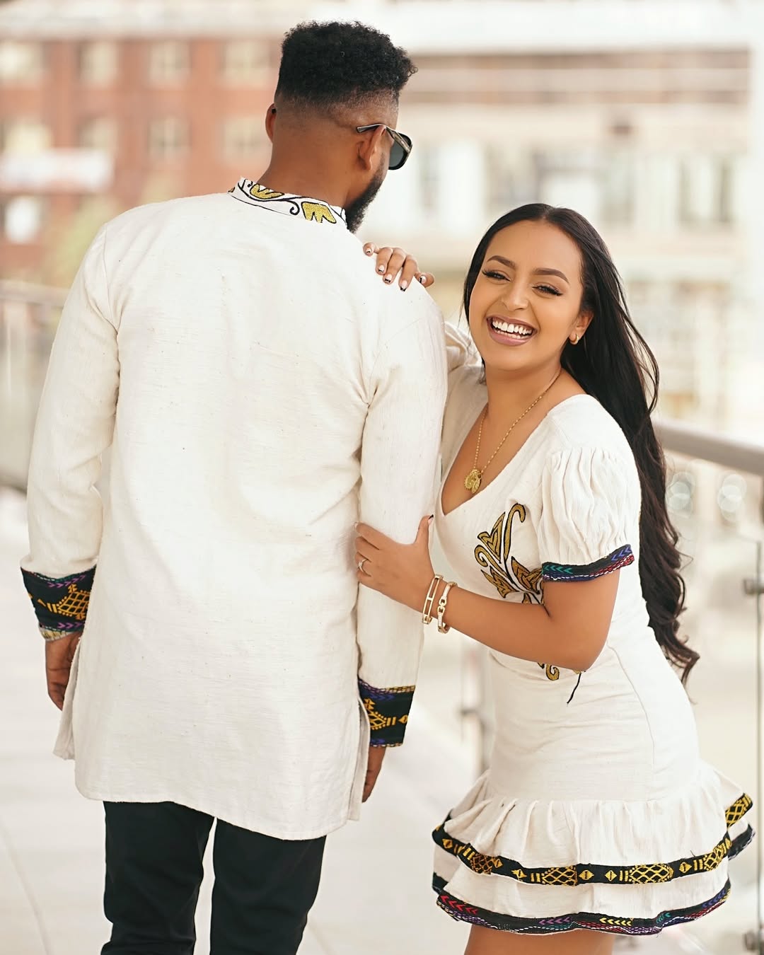 Couple in traditional attire standing close together outdoors. Modern Ethiopian Couple Set Mini Dress & Men’s Habesha Shirt ethgebya gebeya usa habesha kemis mini