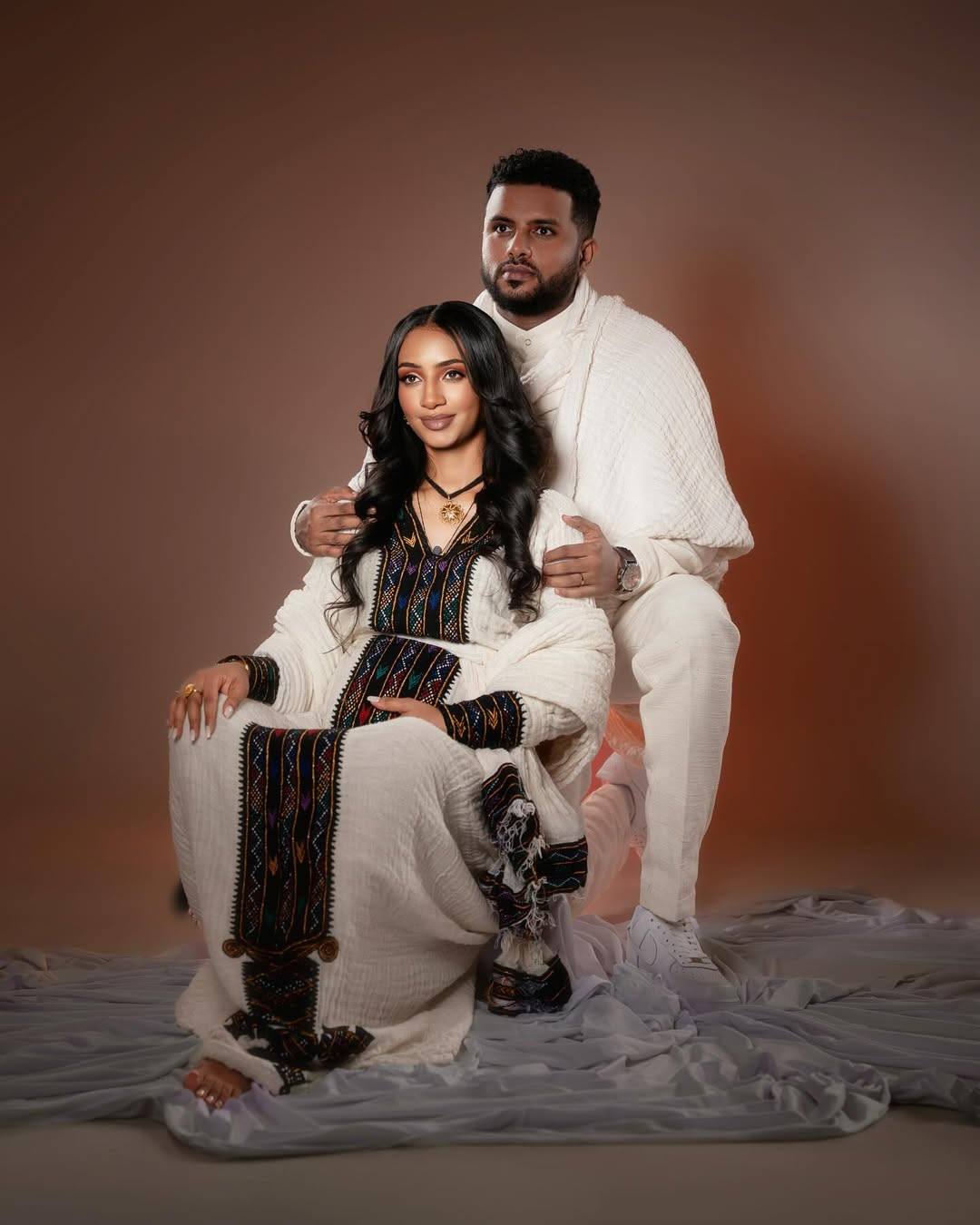 Two people in white and black outfits posing against a brown background Axum Habesha Kemis & Men’s White Shirt with Gabi Ethiopian Couple Set ethgebya gebeya usa habesha kemis men 