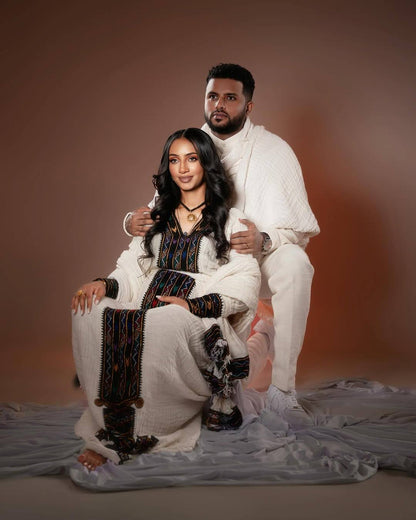 Two people in white and black outfits posing against a brown background Axum Habesha Kemis & Men’s White Shirt with Gabi Ethiopian Couple Set ethgebya gebeya usa habesha kemis men 