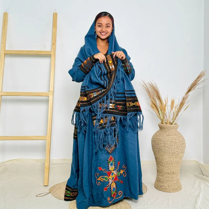 Woman wearing a blue embroidered dress with a colorful scarf in a minimalistic setting. Dark Blue Raya Cultural Dress Handwoven Ethiopian Habesha Kemis ethgebya gebeya usa habesha kemis