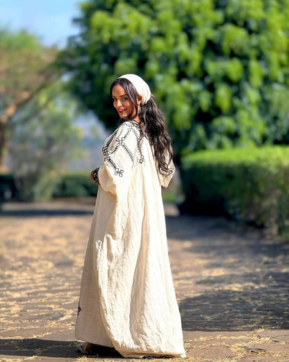 Woman in a long, light-colored dress with intricate patterns walking outdoors. Gonder Habesha Kemis New Relaxed Ethiopian Traditional Dress ethgebya gebeya usa gondar habesha kemis