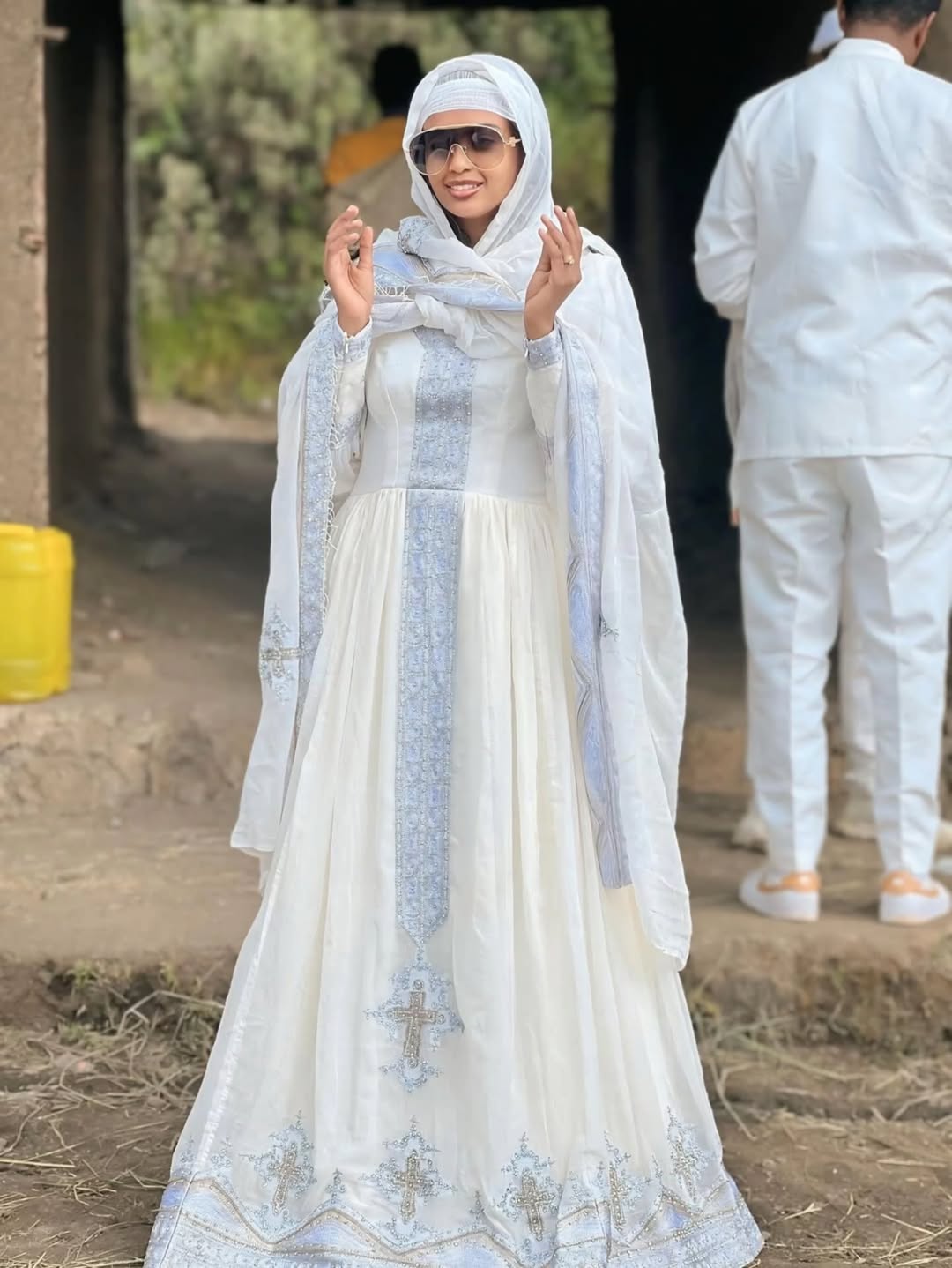 Woman in a white and light blue traditional outfit with a headscarf, standing outdoors. Silver Modern Habesha Couple Outfit Matching Ethiopian Attire ethgebya gebeya usa habesha kemis