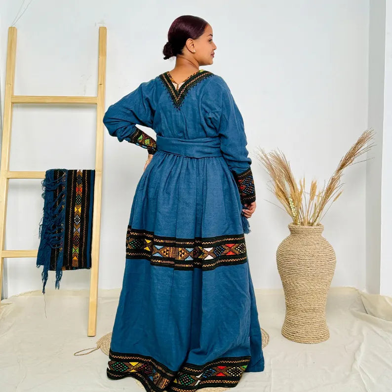 Woman wearing a blue dress with intricate patterns in a minimalistic setting. Dark Blue Raya Cultural Dress Handwoven Ethiopian Habesha Kemis ethgebya gebeya usa habesha kemis