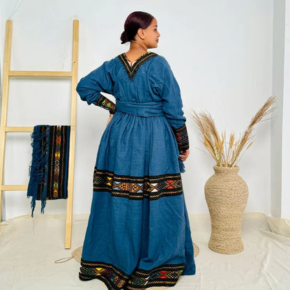 Woman wearing a blue dress with intricate patterns in a minimalistic setting. Dark Blue Raya Cultural Dress Handwoven Ethiopian Habesha Kemis ethgebya gebeya usa habesha kemis
