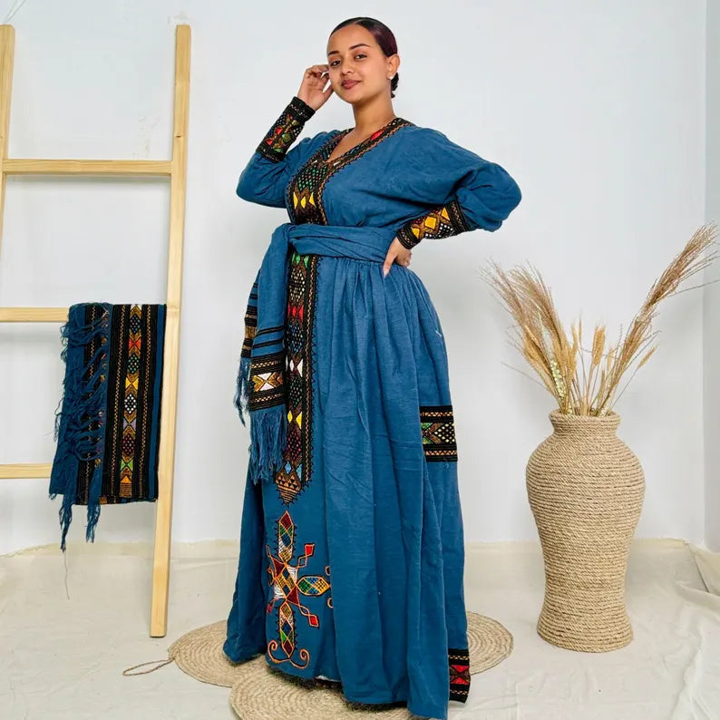 Woman wearing a blue embroidered dress standing in a room with decorative elements. Dark Blue Raya Cultural Dress Handwoven Ethiopian Habesha Kemis ethgebya gebeya usa habesha kemis