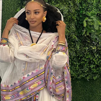 Woman in traditional attire with colorful patterns against a green leafy background Rose Gold Zuria Habesha Kemis Modern Ethiopian Traditional Dress ethgebya gebeya usa habesha kemis