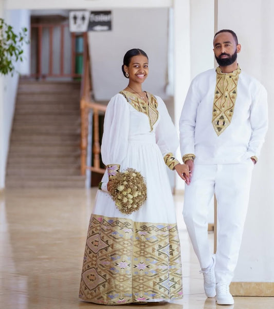 Man and woman holding hands in formal white and gold outfits indoors.