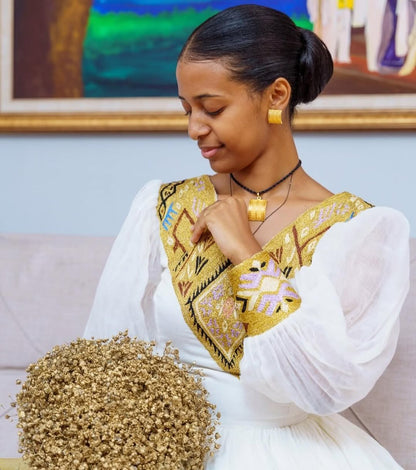 Woman wearing a traditional outfit with gold embroidery, sitting on a couch.