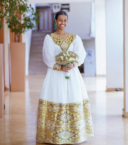 Woman in a white and gold traditional dress holding flowers indoors.