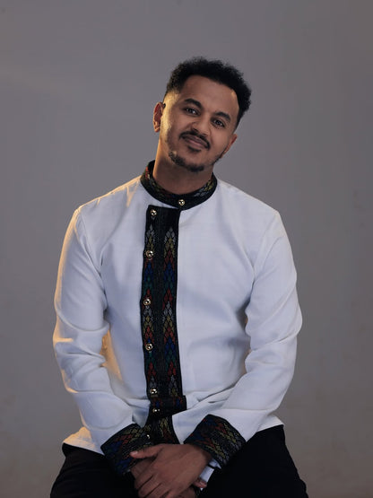 Man wearing a traditional outfit with a white shirt and black and colorful details on a gray backgroundEthiopian Men’s Shirt | Handwoven Tilf Embroidery New Habesha Fashion