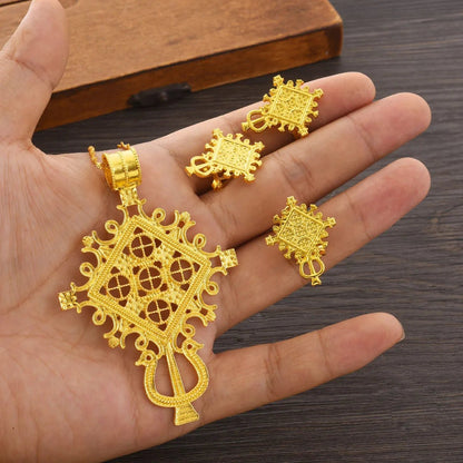 Gold jewelry set including a pendant and earrings on a hand against a wooden background