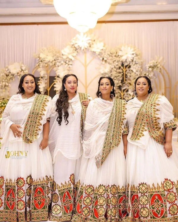 Four women in traditional white and gold dresses standing together in a decorated indoor setting.