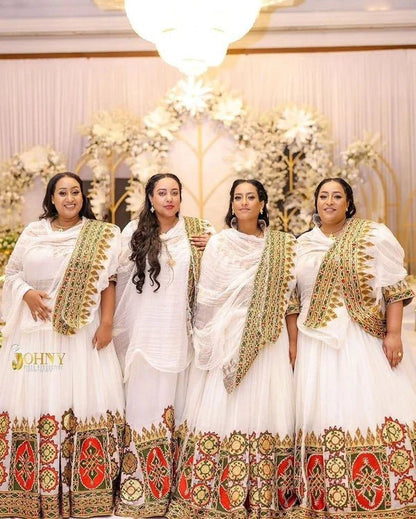 Four women in traditional white and gold dresses standing together in a decorated indoor setting.