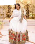 Woman in a white and patterned traditional outfit standing in an elegant indoor setting.