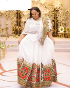 Woman in a white and patterned traditional outfit standing in an elegant indoor setting.