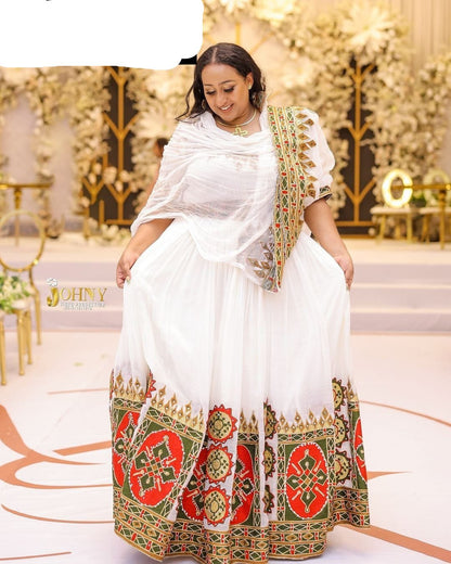 Woman in a white and patterned traditional outfit standing in an elegant indoor setting.