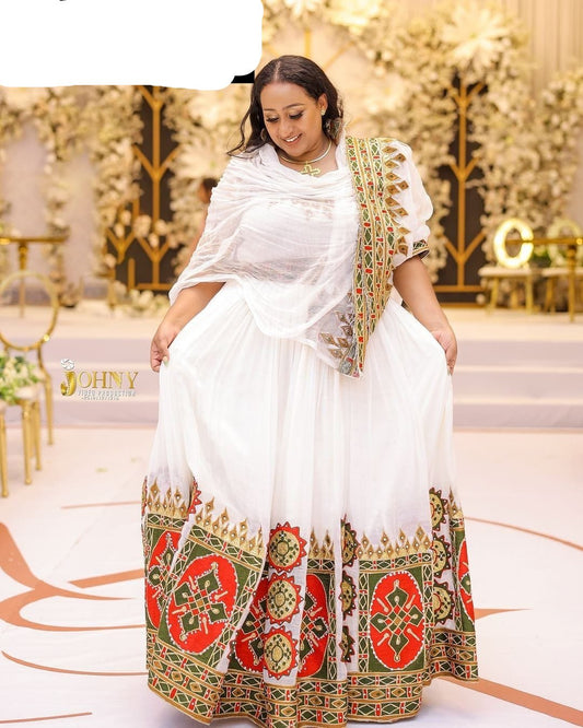 Woman in a white and patterned traditional outfit standing in an elegant indoor setting.