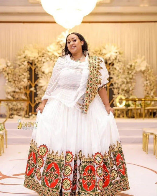 Woman in a white traditional outfit with colorful patterns in an elegant indoor setting.