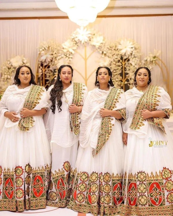 Four women in traditional white and gold dresses with intricate patterns standing together.