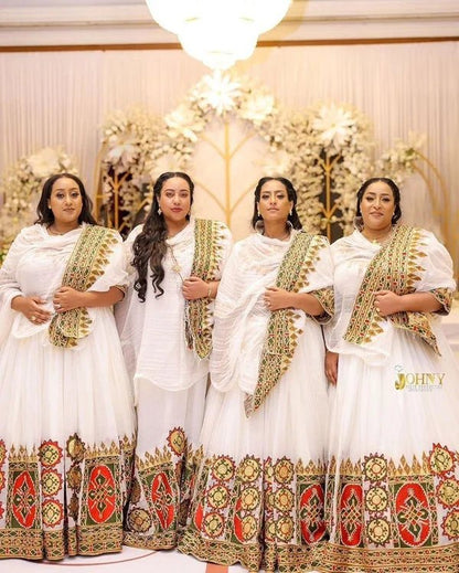 Four women in traditional white and gold dresses with intricate patterns standing together.